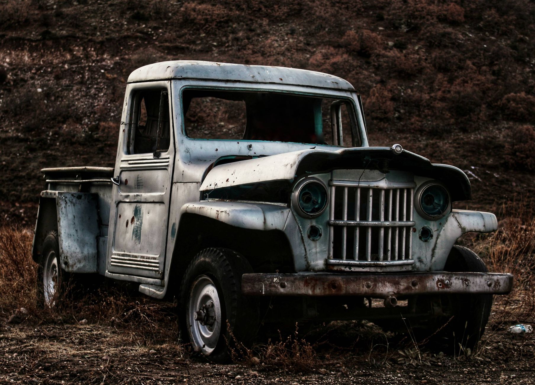 An old, abandoned pickup truck rusting in a dry field, evoking a sense of nostalgia and decay