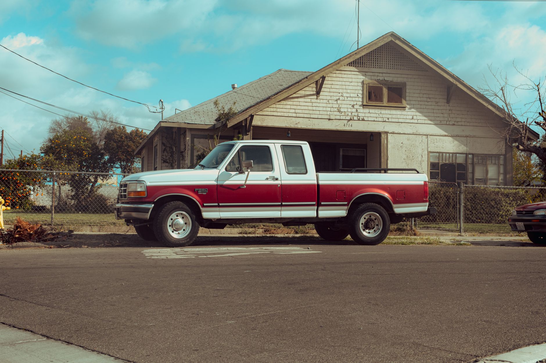 Classic red and white pickup truck parked on an empty street in front of a rustic house